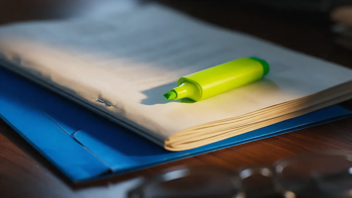 Close em um contrato de consórcio impresso sobre a mesa, com marca-texto verde e pasta azul ao lado